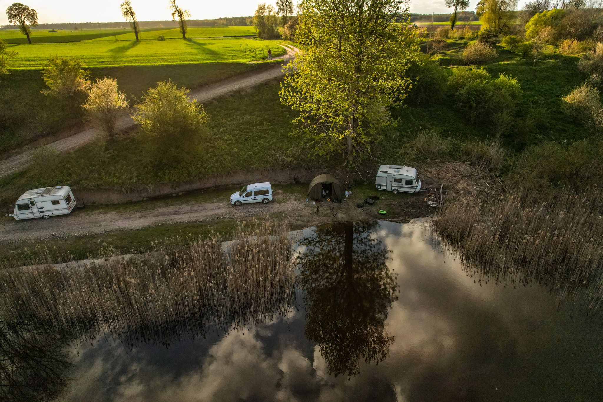 A serene aerial shot of a lakeside campsite featuring caravans and lush greenery.