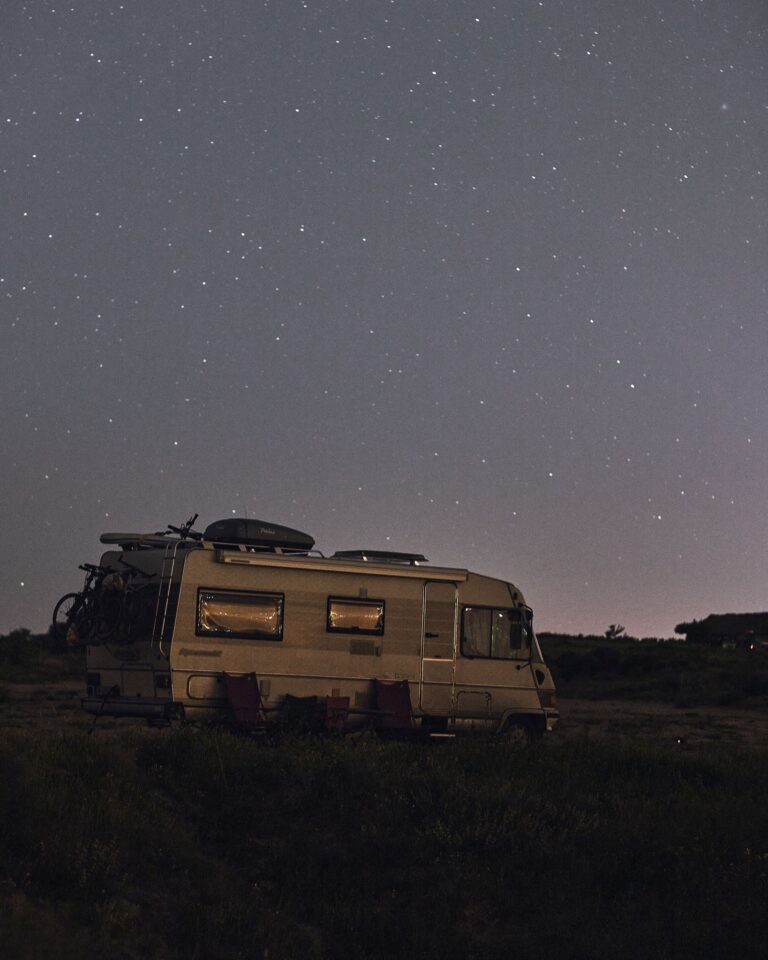 A serene night sky full of stars over a parked camper in a quiet wilderness setting.